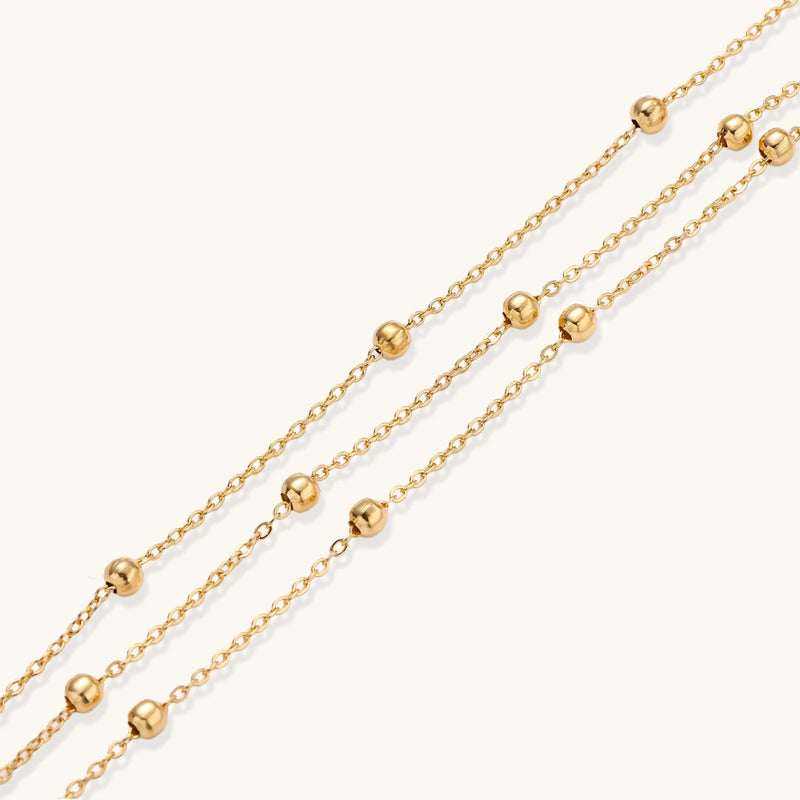 Three-strand gold-plated bracelet with clustered ball beads and adjustable clasp on cream background